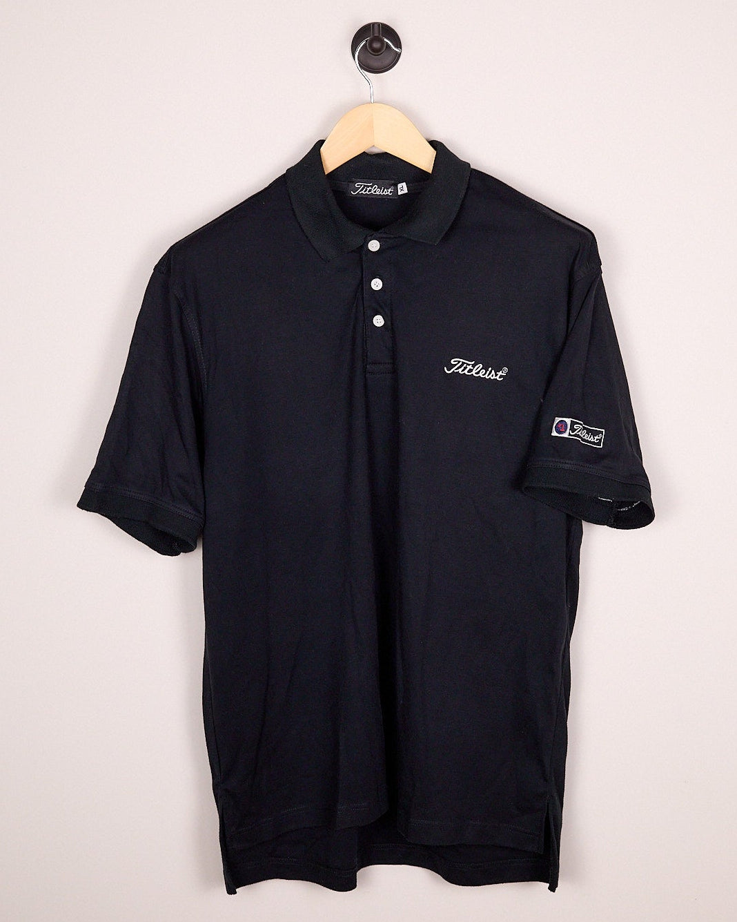 Black polo shirt on a hanger against a light gray background